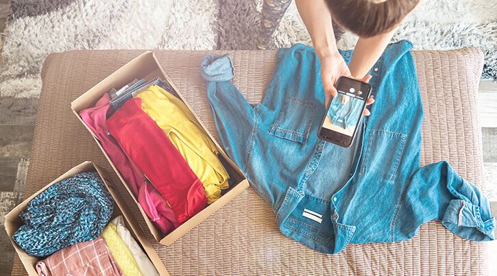 A girl takes a photo of a denim shirt laid out on a cushion 