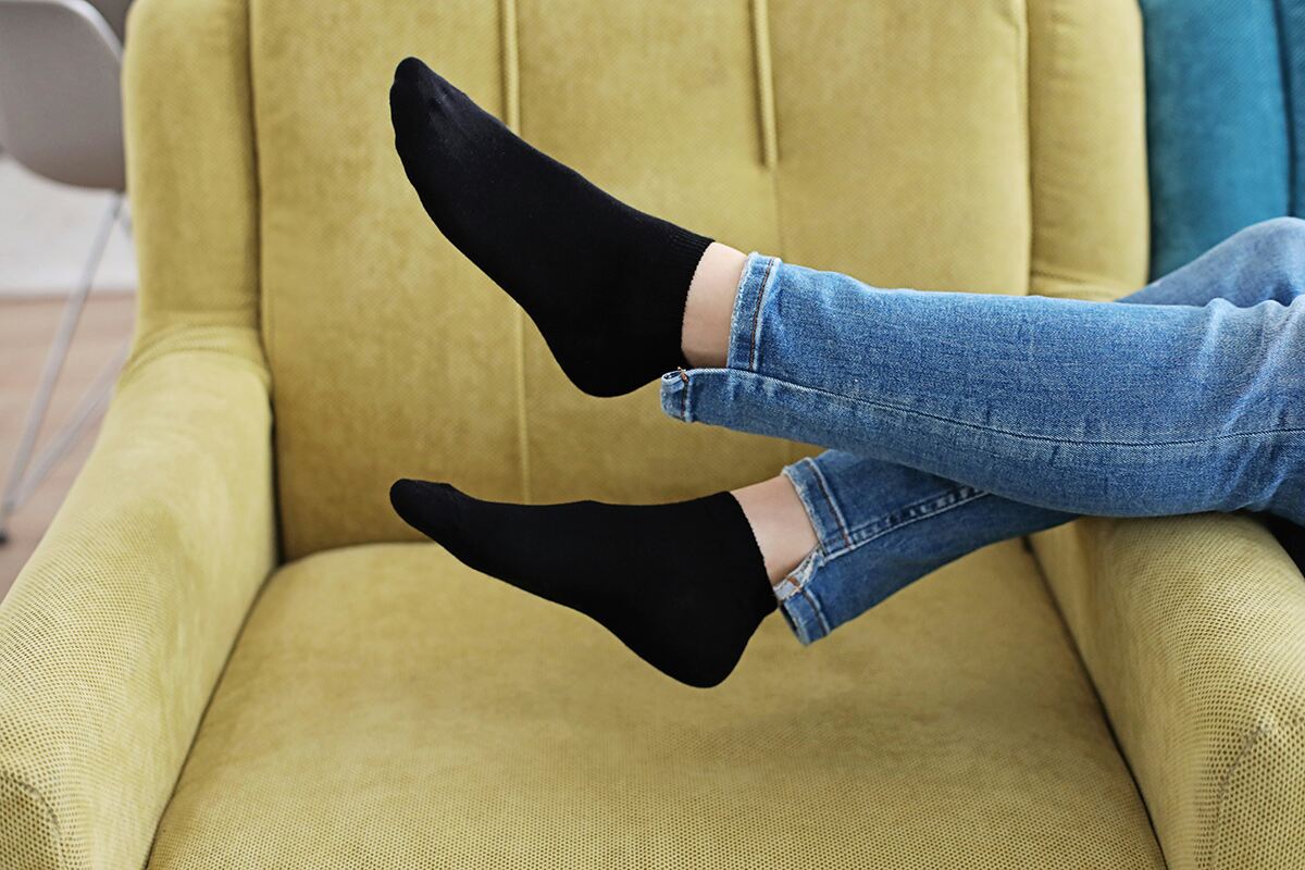 A pair of legs and feet up on a chair, wearing jeans and ankle/trainer socks