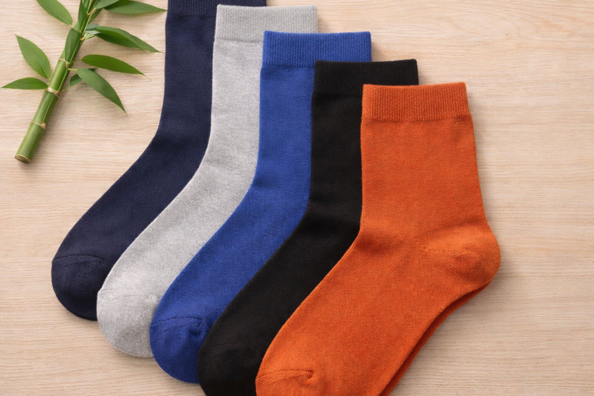 Bamboo socks in navy, grey, blue, black and orange laid out on a wooden surface with a bamboo stem.