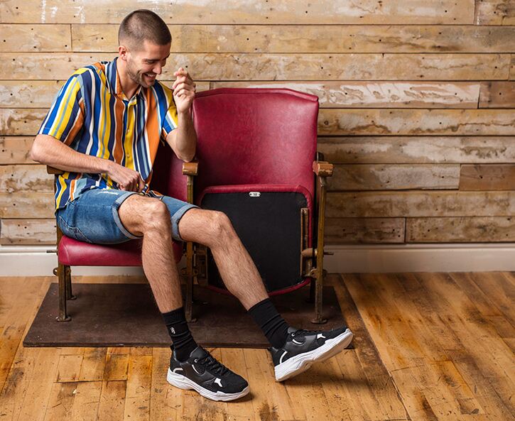 Man wearing a casual shirt and denim shorts with black sports socks and trainers