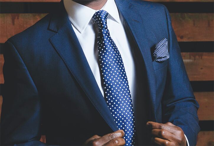 Man in navy suit with white shirt and blue polka dot tie and pocket square