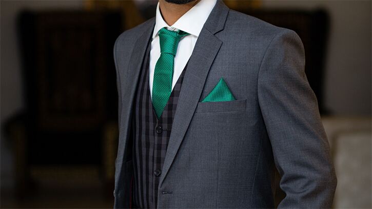 Man in dark grey suit with check waistcoat and emerald green tie and pocket square